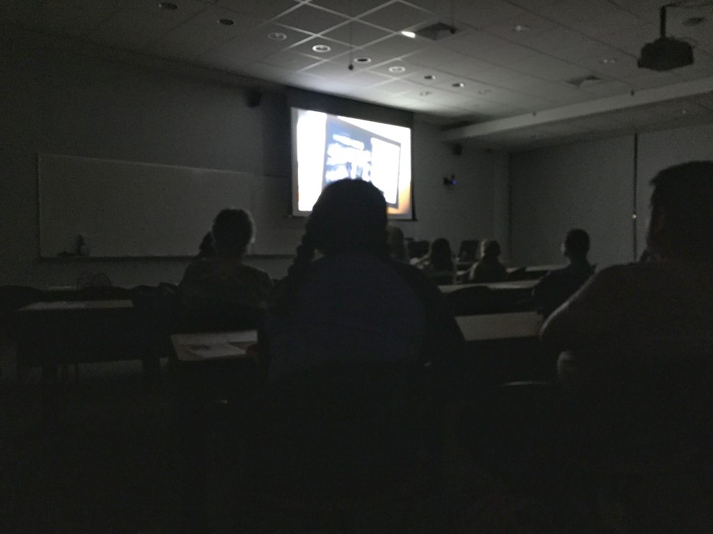 A scene from Snowpiercer is projected onto a screen in a dark classroom with silhouettes of event attendees in the foreground.