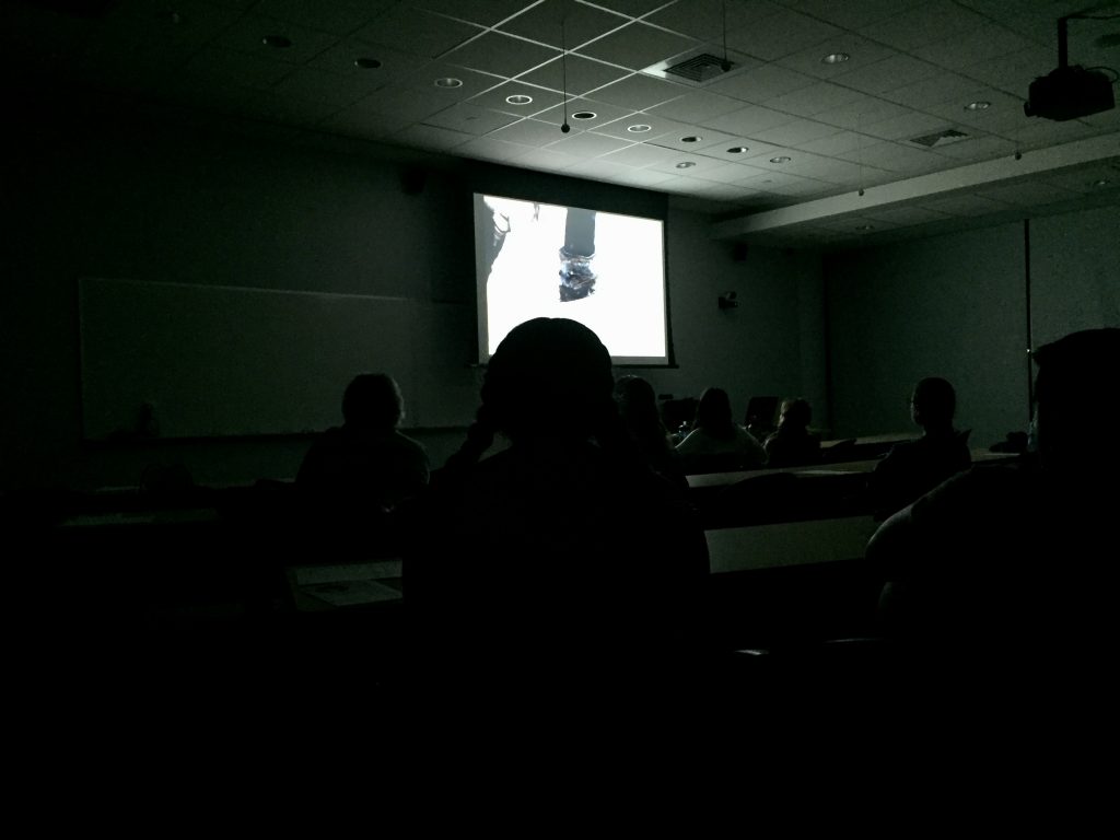 A scene from Snowpiercer is projected onto a screen in a dark classroom with silhouettes of event attendees in the foreground.